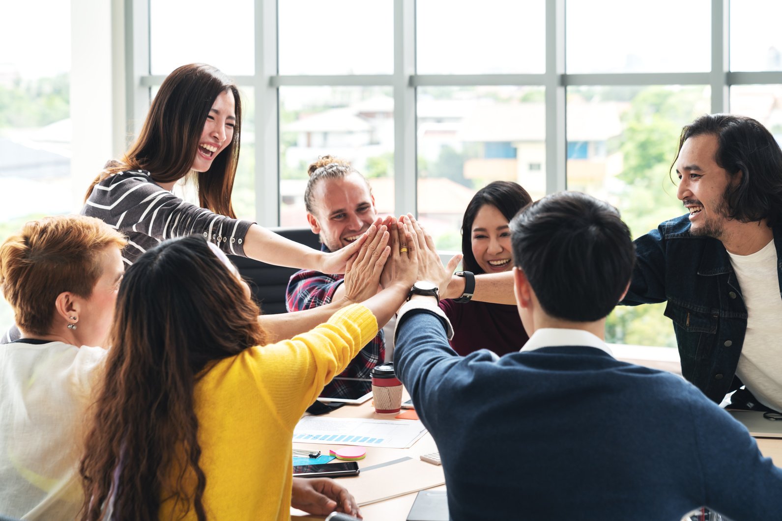 group of young multiethnic diverse people gesture hand high five, laughing and smiling together in brainstorm meeting at office. Casual business with startup teamwork community celebration concept.